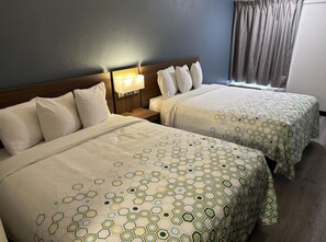 Ein Hotelzimmer mit zwei Betten, jeweils mit einem Bettbezug mit geometrischem Muster, einem Holz-Kopfschild, einem Nachttisch mit Lampe und einem Fenster mit Vorhängen.