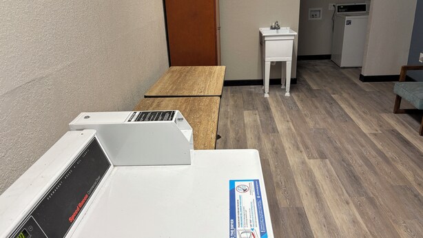 Ein Zimmer mit einem Holztisch, einem weißen Trockner, einem kleinen Spülbecken und einer Mikrowelle.