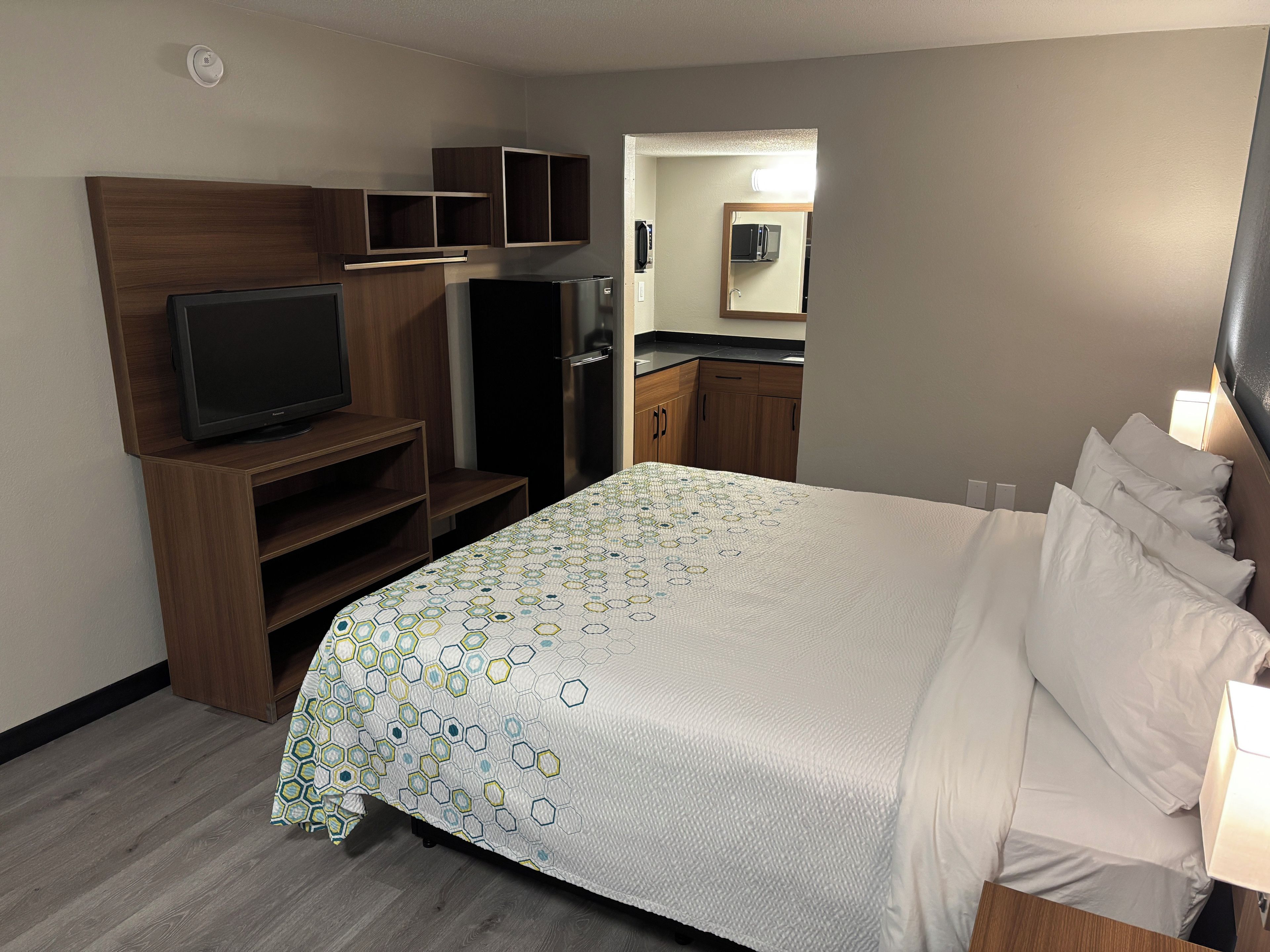 Una camera d'albergo con un letto, una televisione, un armadio e un bagno visibile attraverso una porta aperta.