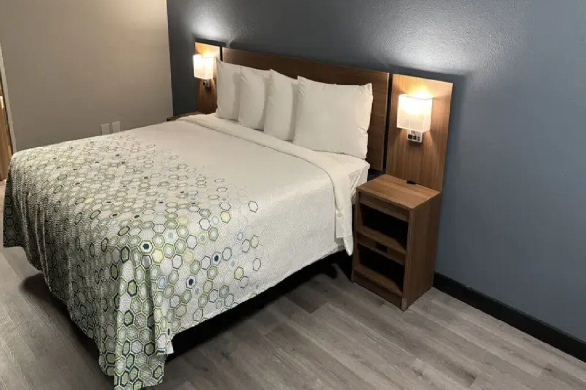 Une chambre d’hôtel avec un grand lit, deux lampes de chevet, une table de chevet en bois et une couvre-lit à motifs.