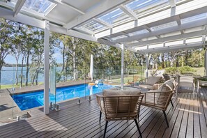 A covered outdoor area with a pool, wooden deck, and seating.