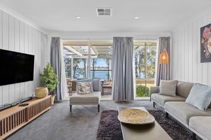 A modern living room with a flat-screen TV, a sofa, a coffee table, and a view of the outdoors.