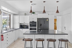Una cocina moderna con armarios blancos, una isla central con taburetes, electrodomésticos de acero inoxidable e iluminación colgante.