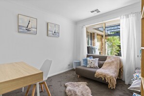 Una sala moderna con una mesa de comedor de madera, un sofá gris con una manta y dos cuadros en la pared.