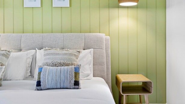 Een slaapkamer met een bed, kussens, een nachtkastje en twee ingelijste foto's aan de muur.