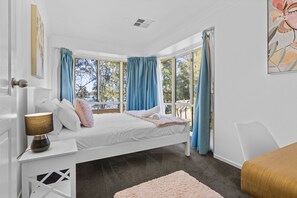 A bedroom with a bed, a bedside table, a lamp, and a window with curtains.