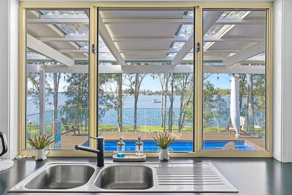 A kitchen with a large window overlooking a pool and a body of water.
