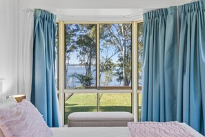 A bedroom with a large window, a bed, and a view of a lake and trees.