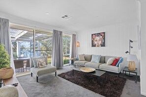 A modern living room with a sofa, armchair, coffee table, and a painting on the wall.