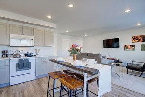 A modern kitchen with a central island, bar stools, a dining table set for four, and a television mounted on the wall. - NEW Mountain Game Room Getaway (Bozeman)