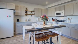 Een moderne keuken met lichte kastjes, een centraal eiland met krukken, een magnetron en een vaas met bloemen.