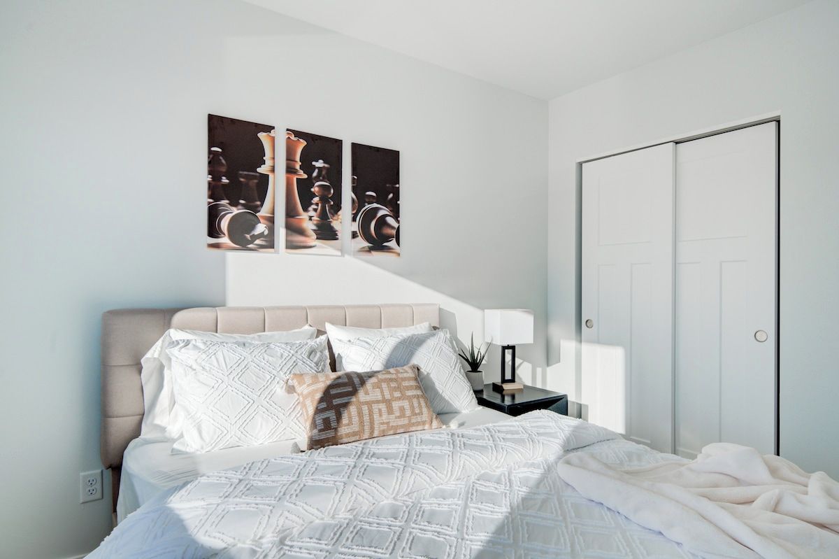 Een slaapkamer met een bed, kussens, een nachtkastje, een lamp en een kledingkast.