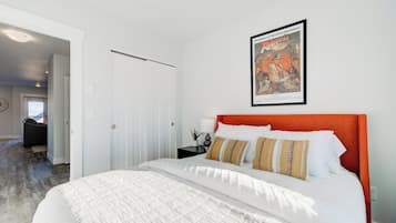 A bedroom with a bed, a framed movie poster, a white door, and a hallway leading to another room.