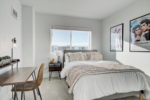 A bedroom with a bed, a desk, a chair, a window, and two posters on the wall.