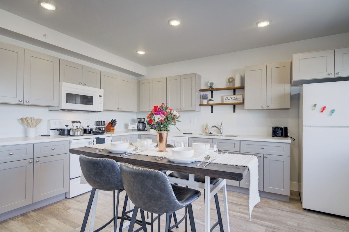 A modern kitchen with white cabinets, a central island with bar stools, a microwave, and a refrigerator.