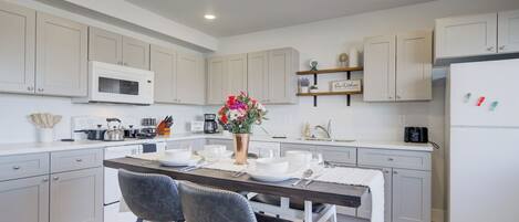 A modern kitchen with white cabinets, a central island with bar stools, a microwave, and a refrigerator.