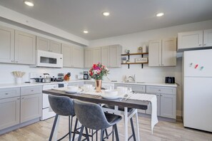 Una cocina moderna con armarios blancos, una isla central con taburetes y un microondas, además de un refrigerador.