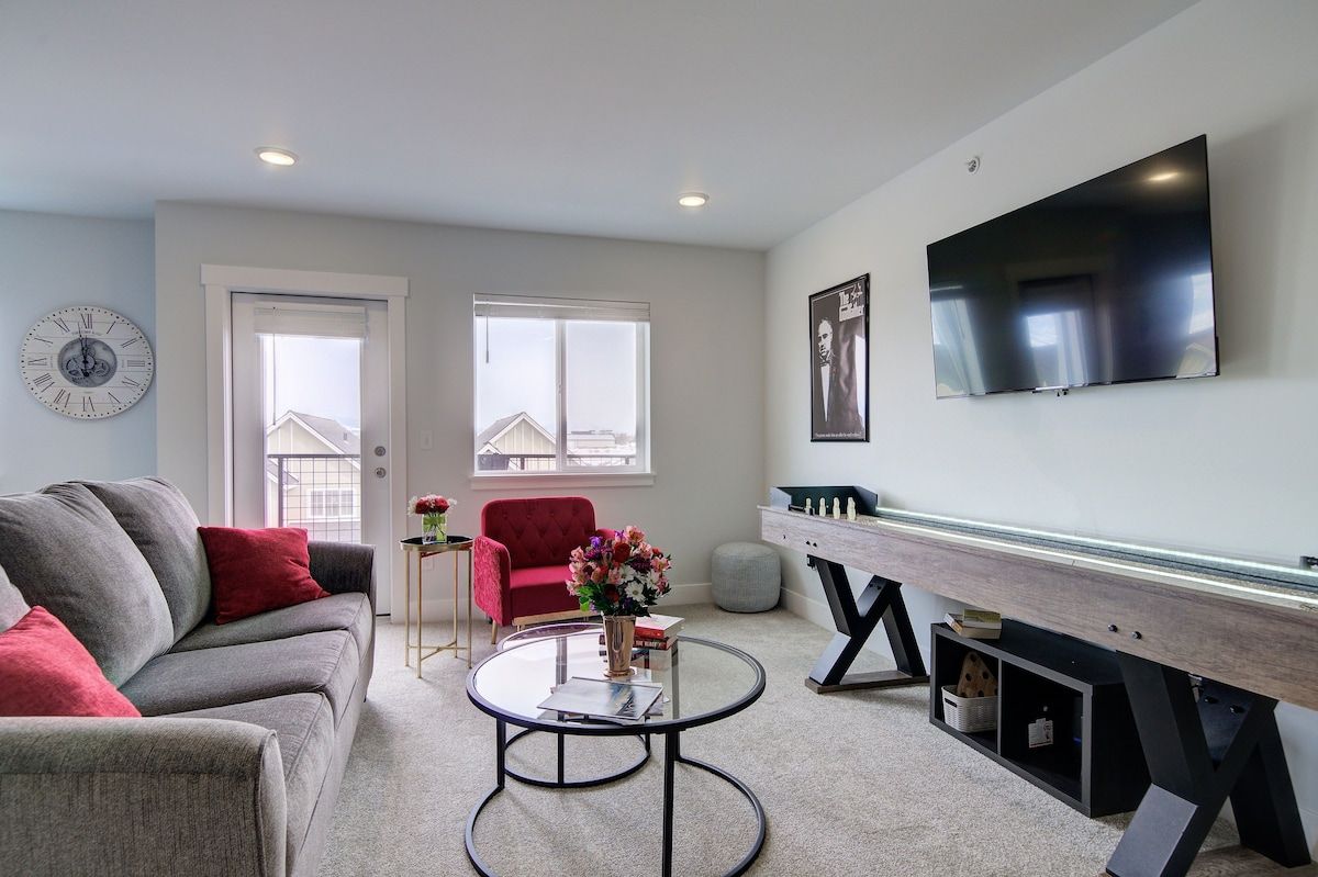 A modern living room with a grey sofa, a red armchair, a round coffee table, and a flat-screen TV mounted on the wall.