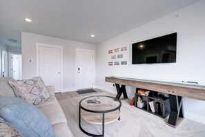 Un salon moderne avec un canapé, une table basse, un téléviseur fixé au mur et une bibliothèque.