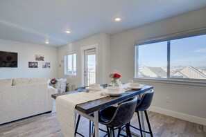 A dining area with a table set for four, a sofa, and a view of the cityscape through large windows. - NEW Mountain Views | Hot Springs | Truck Stop (Bozeman)