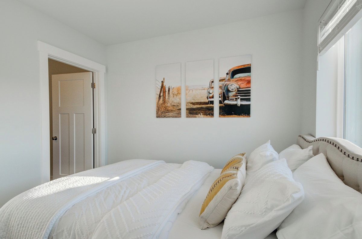 Ein Schlafzimmer mit einem Bett, weißer Bettwäsche und einer Wand mit drei gerahmten Bildern.