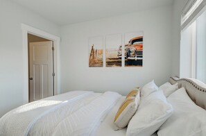 A bedroom with a bed, white bedding, and a wall with three framed pictures. - NEW Mountain Views | Hot Springs | Truck Stop (Bozeman)