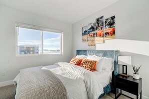 A bedroom with a bed, a nightstand, a window, and wall art.