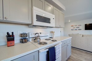A compact kitchen with a microwave, stove, and kettle.