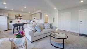 A modern living room with a sofa, coffee table, and kitchen area in the background. - NEW Mountain Views | Hot Springs | Truck Stop (Bozeman)
