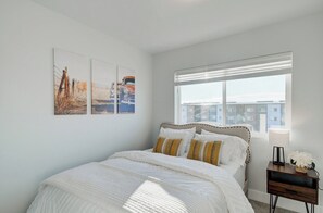 A bedroom with a bed, a nightstand, a window, and wall art.