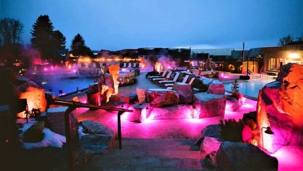 A heated outdoor pool area with stone seating and a wooden deck. - NEW Mountain Views | Hot Springs | Truck Stop (Bozeman)