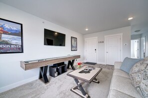 A modern living room with a glass-top coffee table, a sofa, a mounted flat-screen TV, and a framed picture on the wall.