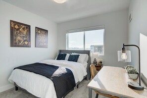A bedroom with a bed, a desk, a chair, a window, and two wall-mounted artworks.