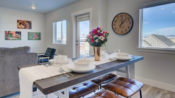 A dining area with a table set for two, a clock on the wall, and artwork on the walls. - 2 Adjoining Condos Rent Together (Bozeman)