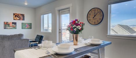A dining area with a table set for two, a clock on the wall, and artwork on the walls.