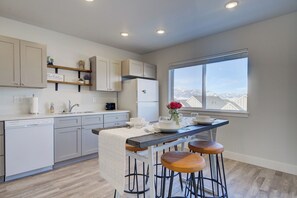 A modern kitchen with a central island, bar stools, and a view of mountains through a large window.