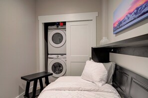 A bedroom with a bed, a bench, a washing machine, and a painting on the wall. - Cozy Downtown Condo (Bozeman)