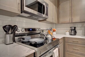 A modern kitchen with stainless steel appliances, including a microwave, stove, and coffee maker. - Cozy Downtown Condo (Bozeman)