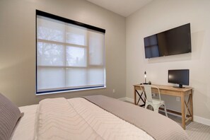 A bedroom with a bed, a desk, a chair, a television, and a window with blinds. - Cozy Downtown Condo (Bozeman)