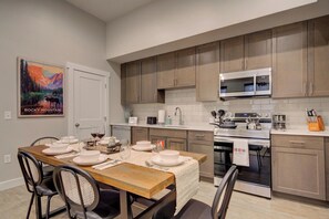 A modern kitchen with wooden cabinets, a stainless steel microwave, and a dining area set for a meal. - Cozy Downtown Condo (Bozeman)