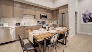 A modern kitchen with wooden cabinets, stainless steel appliances, and a dining area set for four. - Cozy Downtown Condo (Bozeman)
