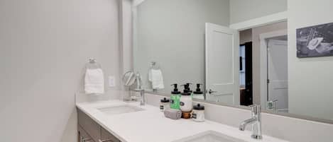 Un baño moderno con dos lavamanos, un espejo grande y una puerta que da a otra habitación.