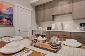 A dining area with a wooden table set for two, white plates, glasses, and a tray with a bottle. - Cozy Downtown Condo (Bozeman)