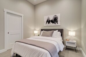 A bedroom with a bed, two bedside lamps, a door, and a wall-mounted picture of cows. - Cozy Downtown Condo (Bozeman)