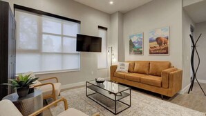 A modern living room with a sofa, coffee table, and a flat-screen TV mounted on the wall. - Cozy Downtown Condo (Bozeman)