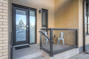 A building entrance with a glass door, a metal gate, and a small outdoor seating area with chairs. - Cozy Downtown Condo (Bozeman)