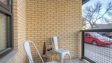 A brick wall with two white chairs and a bottle of wine on a wooden stool.