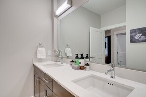 Une salle de bain moderne avec deux lavabos, un grand miroir et une porte donnant sur une autre pièce.