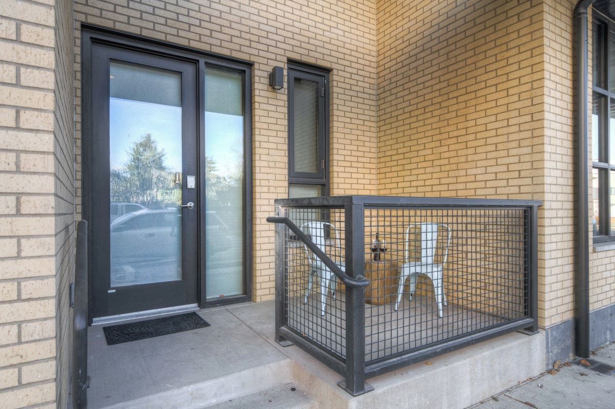 A building entrance with a glass door, a metal gate, and a small outdoor seating area.