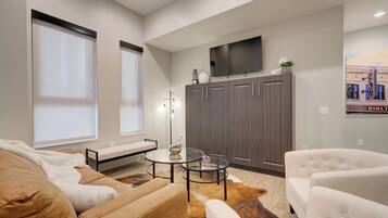 A modern living room with a sofa, armchairs, a coffee table, and a flat-screen TV mounted on the wall.